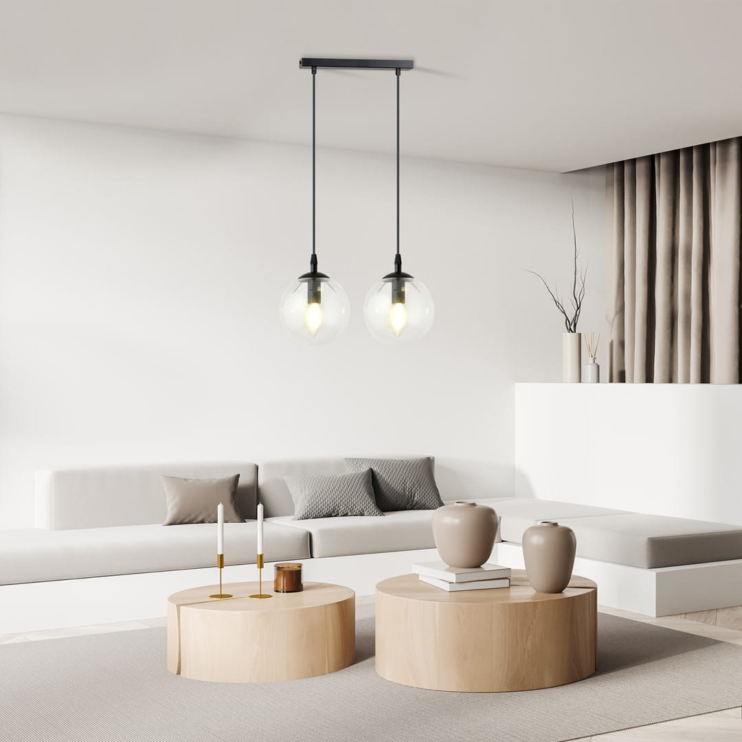 Lampa wisząca Cosmo 2-punktowa z przezroczystymi kloszami, zawieszona na czarnych linkach. Klosze o okrągłym kształcie, z widocznymi żarówkami, w nowoczesnym wnętrzu z jasnymi meblami i naturalnymi dodatkami.
