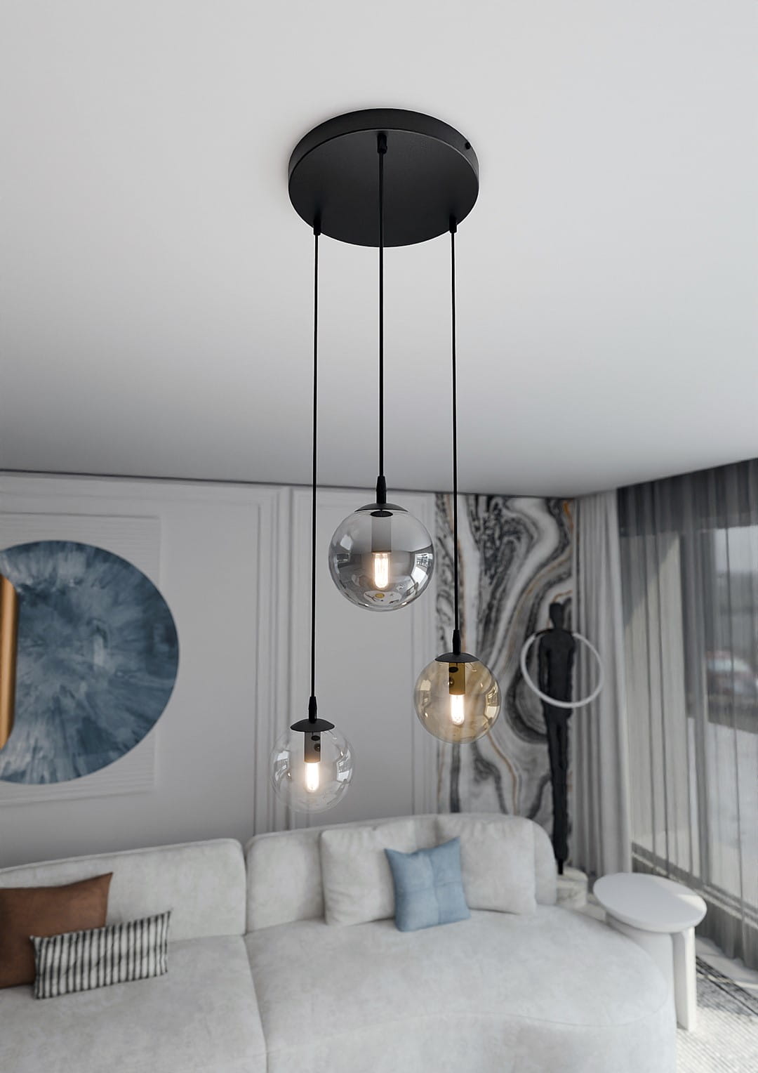 Lampa wisząca Cosmo Premium 3-punktowa w kolorze multikolorowym, składająca się z trzech przezroczystych kul w różnych odcieniach, zawieszona na czarnych linkach. Zainstalowana pod sufitem, w nowoczesnym wnętrzu z jasną sofą i dekoracjami.