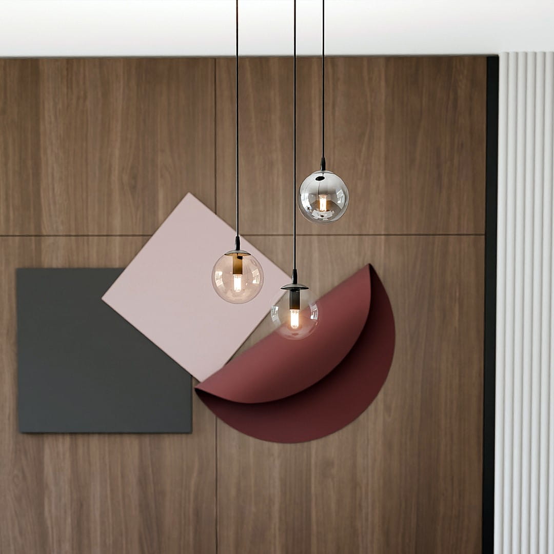 Lampa wisząca Cosmo Premium 3-punktowa w kolorach multikolorowych. Składa się z trzech okrągłych kloszy w różnych odcieniach, zawieszonych na cienkich, czarnych linkach. W tle widoczne geometryczne dekoracje na drewnianej ścianie.