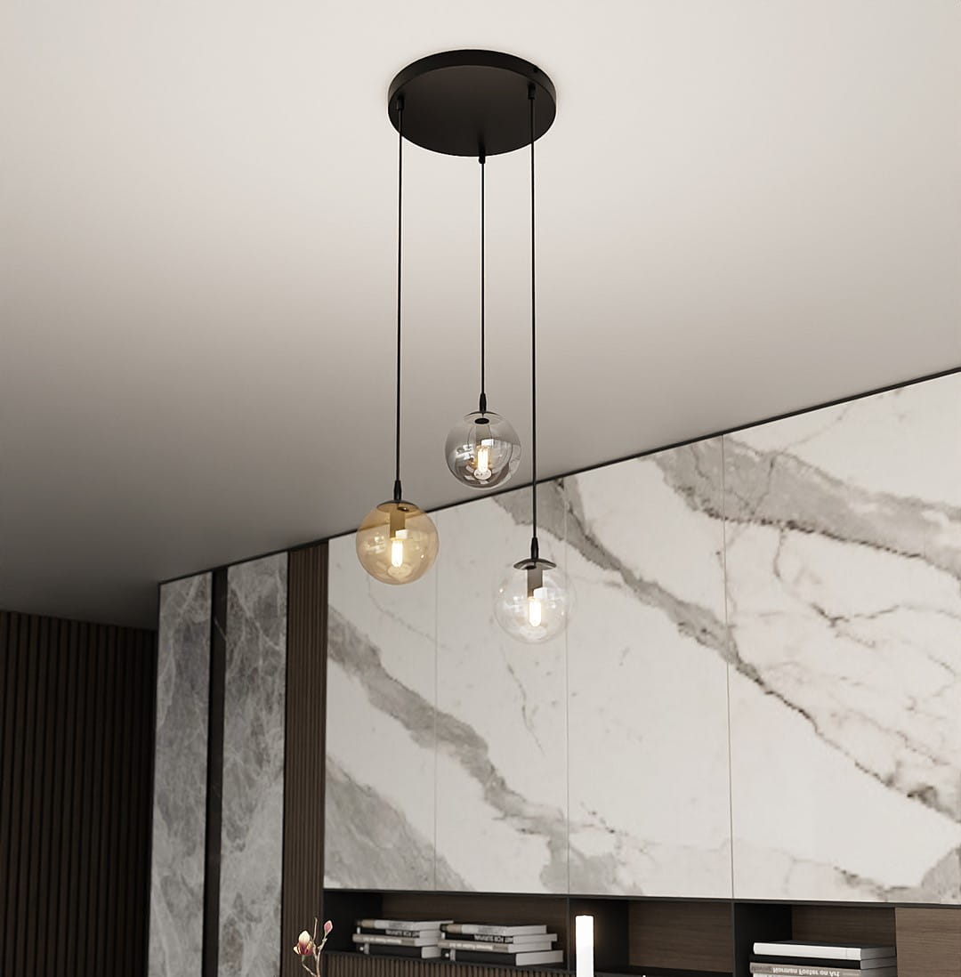 Lampa wisząca Cosmo Premium 3-punktowa, składająca się z trzech szklanych kul w różnych kolorach (przezroczysta, miodowa, szara), zawieszona na czarnych linkach. Montowana na okrągłej podstawie, w nowoczesnym wnętrzu z marmurowymi akcentami.