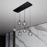 Lampa wisząca Cosmo 6-punktowa w kolorze grafitowym. Posiada sześć przezroczystych kulowych kloszy zawieszonych na czarnych przewodach, mocowanych do prostokątnej podstawy. Tło w odcieniach szarości z marmurowym wzorem.