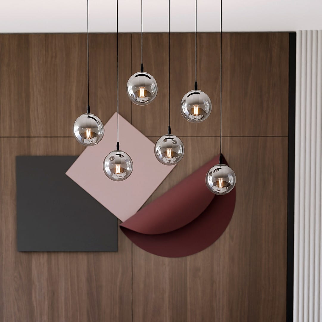 Lampa wisząca Cosmo 6-punktowa w kolorze grafitowym, z sześcioma okrągłymi kloszami w metalicznym wykończeniu, zawieszona na cienkich czarnych linkach. Tło stanowi drewniana ściana oraz geometryczne elementy w neutralnych kolorach.