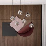 Lampa wisząca Cosmo 6-punktowa w kolorze grafitowym, z sześcioma okrągłymi kloszami w metalicznym wykończeniu, zawieszona na cienkich czarnych linkach. Tło stanowi drewniana ściana oraz geometryczne elementy w neutralnych kolorach.