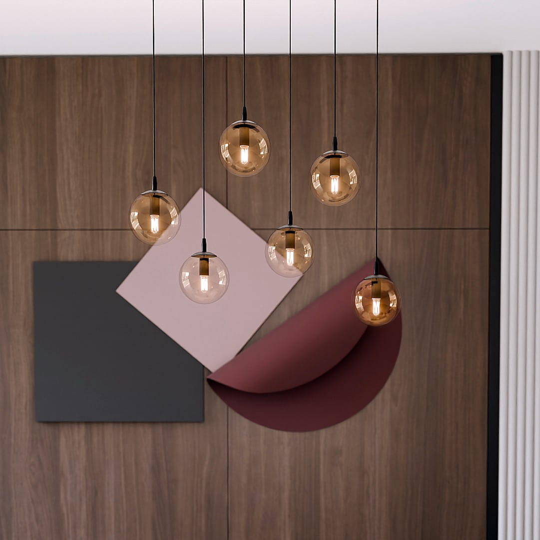Lampa wisząca Cosmo 6-punktowa w kolorze miodowym, z sześcioma okrągłymi kloszami na czarnych zawieszkach. Zawieszona w nowoczesnym wnętrzu z drewnianą ścianą i geometrycznymi dekoracjami w odcieniach różu i szarości.