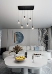 Lampa wisząca Cosmo 6-punktowa, transparentna, z sześcioma kulistymi kloszami zawieszonymi na czarnych linkach z metalowym stelażem. Ujęcie z góry, w nowoczesnym wnętrzu z jasną sofą i dekoracyjnymi elementami.