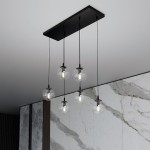 Lampa wisząca Cosmo 6-punktowa z sześcioma przezroczystymi kloszami w kształcie kul, zawieszona na cienkich czarnych kablach. Montaż na prostokątnej, czarnej podstawie. Tło w odcieniach szarości z marmurowym wzorem.