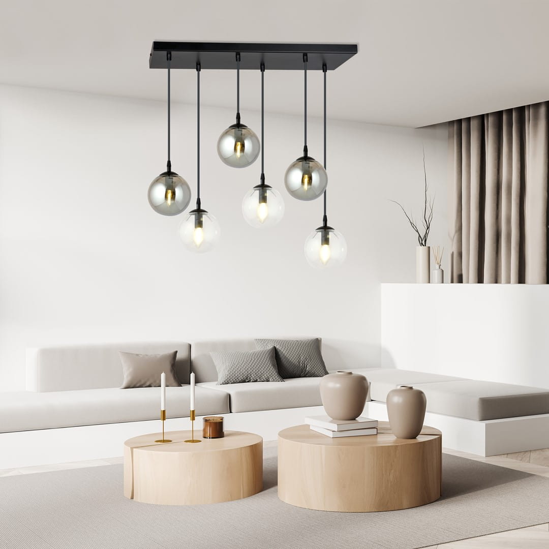 Lampa wisząca Cosmo mix2, 6-punktowa, z sześcioma przezroczystymi kulami na czarnych kablach, zamontowana na prostokątnej podstawie. Produkt wiszący nad okrągłymi stolikami w nowoczesnym wnętrzu.