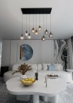 Lampa wisząca Cosmo mix 1, 9-punktowa, z czarnym stelażem i przezroczystymi kulistymi kloszami, zawieszona nad okrągłym białym stołem. W tle nowoczesny salon z dekoracjami, w tym obrazem i roślinami.