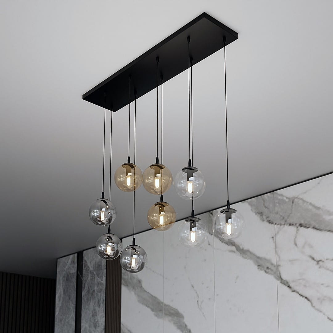 Lampa wisząca Cosmo mix, 9-punktowa, z czarnym stelażem. Składa się z przezroczystych i brązowych kul lampowych zawieszonych na czarnych przewodach. Ujęcie z góry, na tle marmurowej ściany.