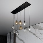 Lampa wisząca Cosmo mix, 9-punktowa, z czarnym stelażem. Składa się z przezroczystych i brązowych kul lampowych zawieszonych na czarnych przewodach. Ujęcie z góry, na tle marmurowej ściany.