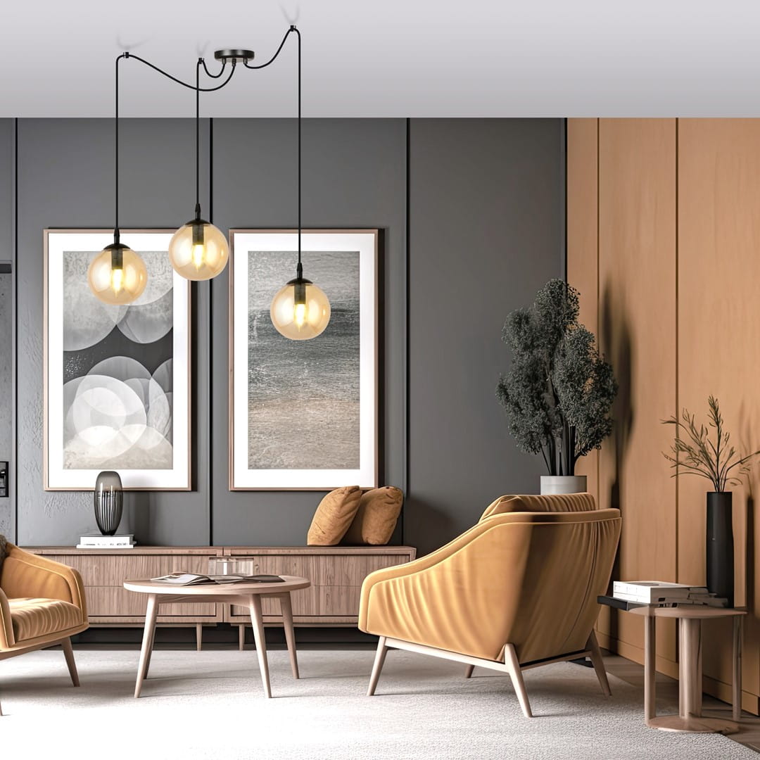 Lampa wisząca Gigi 3-punktowa w kolorze miodowym, z trzema okrągłymi kloszami zawieszonymi na cienkich, czarnych linkach. Ujęcie z góry, w nowoczesnym wnętrzu z meblami w odcieniach drewna i żółtymi fotelami. Tło w stonowanych kolorach.