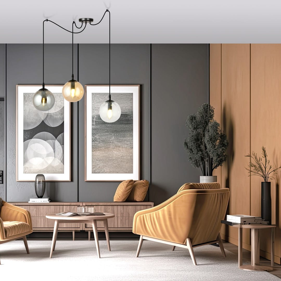 Lampa wisząca Gigi 3-punktowa w kolorze multikolorowym, z trzema szklanymi kloszami w różnych odcieniach, zawieszona na czarnych przewodach. Znajduje się w nowoczesnym salonie z beżowymi meblami i obrazami na ścianie.