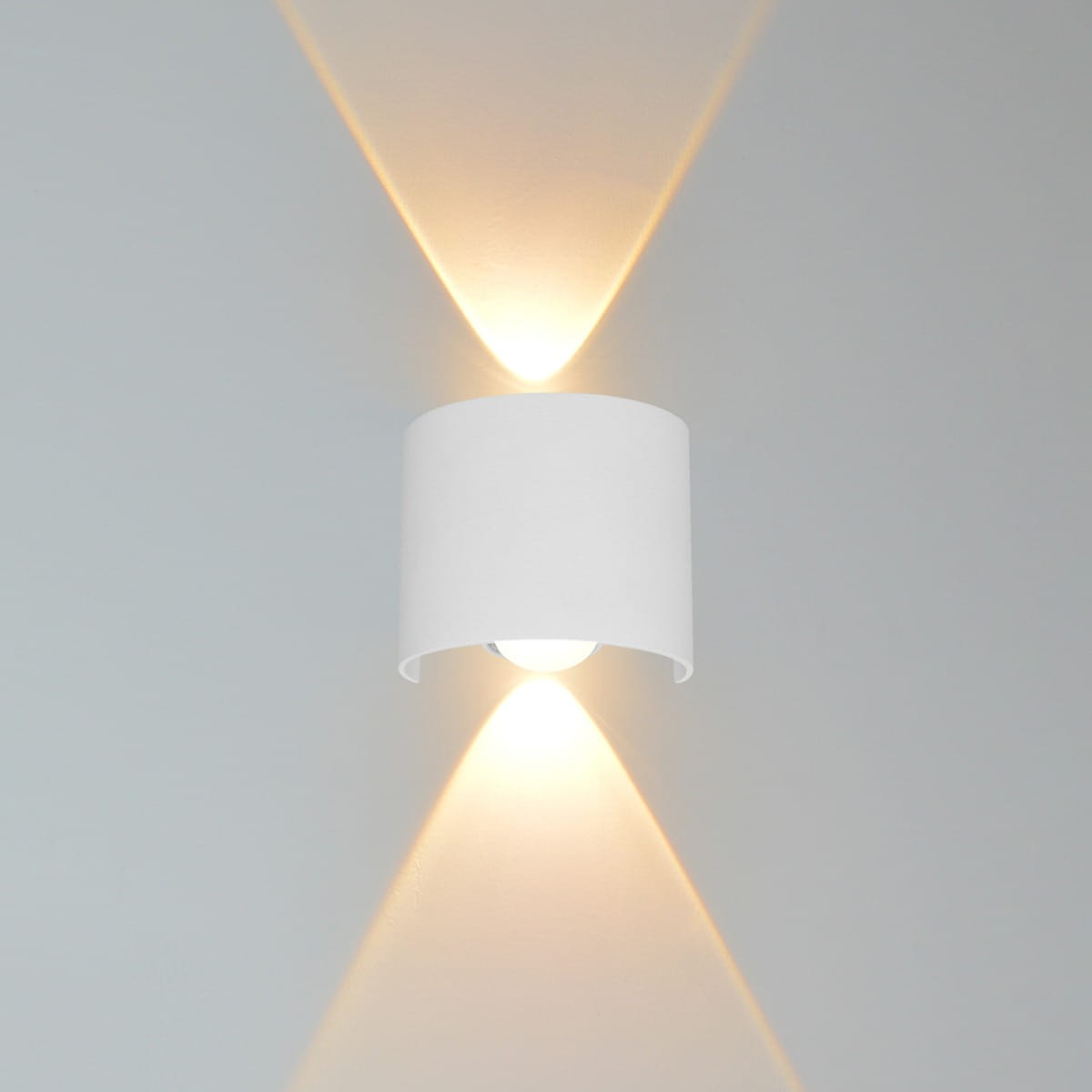 Kinkiet elewacyjny Ortelo 2xLED/2W w kolorze białym, o cylindrycznym kształcie. Zainstalowany na ścianie, emituje światło w górę i w dół, tworząc efekt świetlny. Widoczna żarówka w dolnej części, prosta forma bez dodatkowych zdobień.