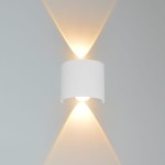 Kinkiet elewacyjny Ortelo 2xLED/2W w kolorze białym, o cylindrycznym kształcie. Zainstalowany na ścianie, emituje światło w górę i w dół, tworząc efekt świetlny. Widoczna żarówka w dolnej części, prosta forma bez dodatkowych zdobień.