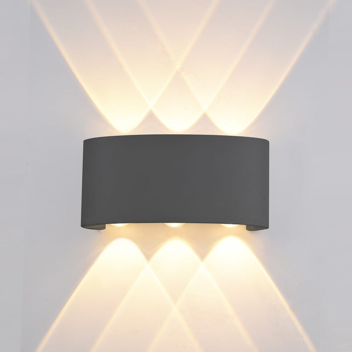 Kinkiet elewacyjny Ortelo 3xLED/6W w kolorze czarnym. Okrągła, matowa obudowa z trzema źródłami światła, emitującymi ciepłe światło, tworzy efektowne wzory na ścianie. Zamontowany na gładkiej, jasnej ścianie.