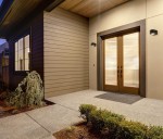 Kinkiet zewnętrzny Pesaro 3K w kolorze czarnym, z jedną diodą LED o mocy 5W i temperaturze barwowej 3000K, zamontowany po obu stronach podwójnych drzwi. Oświetlenie emituje ciepłe światło, podkreślając architekturę budynku.