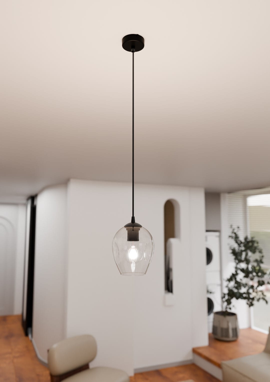 Lampa wisząca Istar 1-punktowa, transparentna, o szklanym kloszu w kształcie dzwonu. Zawieszona na czarnym przewodzie, montowana sufitowo. W tle dwukolorowe wnętrze z drewnianą podłogą i roślinnością.