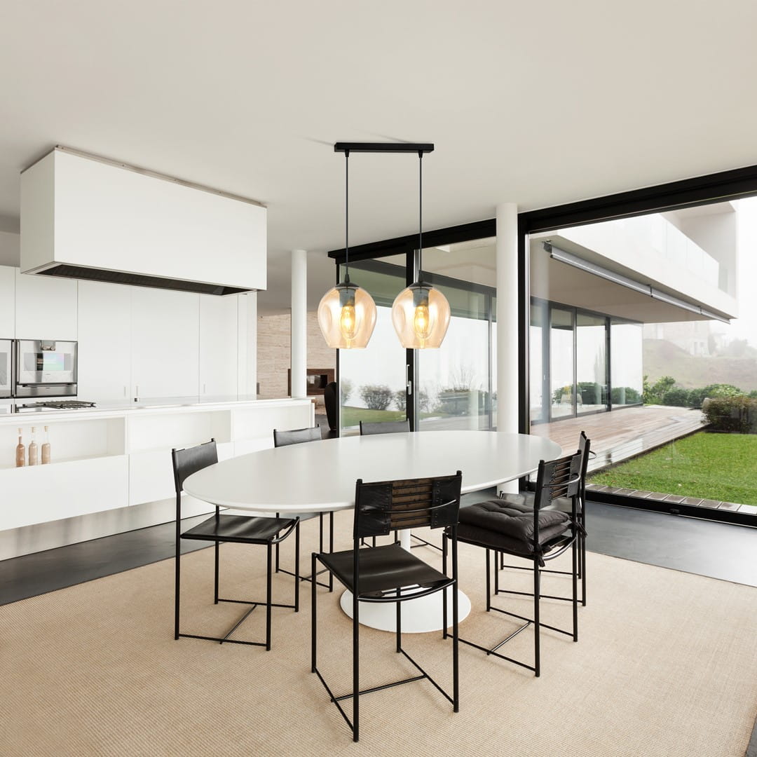 Lampa wisząca Istar 2-punktowa w kolorze miodowym, z podwójnymi kulistymi kloszami, zawieszona na czarnym stelażu. Widoczna w nowoczesnej aranżacji kuchennej nad okrągłym stołem, z czarnymi krzesłami w tle.