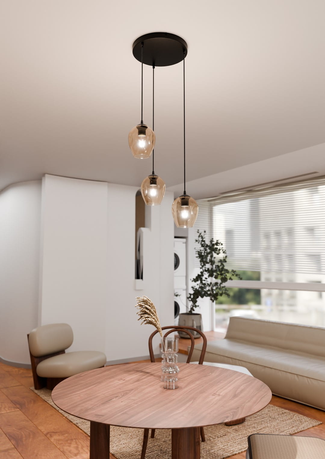 Lampa wisząca Istar Premium 3-punktowa w kolorze miodowym, z trzema szklanymi kloszami o owalnym kształcie, zawieszona na czarnych przewodach. Produkt umieszczony w jasnym wnętrzu nad okrągłym drewnianym stołem.
