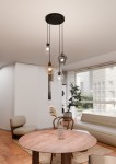 Lampa wisząca Istar Premium mix 4-punktowa, z czterema szklanymi kloszami w różnych kolorach (przezroczysty, brązowy), zawieszona na czarnych linkach. Ujęcie z góry, w nowoczesnym wnętrzu z okrągłym drewnianym stołem i roślinnością w tle.
