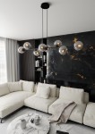 Lampa wisząca Rossi 8-punktowa w kolorze czarnym i grafitowym, zawieszona na dwóch cienkich linkach. Szklane oprawy w kształcie kul, odbijające światło, umieszczone na metalowej konstrukcji. Produkt we wnętrzu z jasną sofą i marmurowym stolikiem.