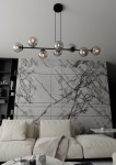 Lampa wisząca Rossi 8-punktowa w kolorze czarnym z grafitowym akcentem, z siedmioma szklanymi kloszami w kształcie kul, zawieszona nad jasną sofą w nowoczesnym wnętrzu. Tło z marmurowymi płytkami podkreśla elegancję produktu.