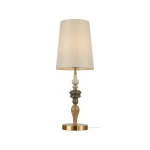 Lampa stołowa Moren z brązowym antycznym wykończeniem, z okrągłą podstawą i dekoracyjnym trzonem w odcieniach beżu, szarości i brązu. Wyposażona w materiałowy klosz w jasnym kolorze, emitującym ciepłe światło. Ujęcie frontalne.