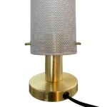Lampa stołowa Tirana z białym kloszem w perforowanym wzorze i złotą podstawą. Ujęcie z boku, pokazujące cylindryczny kształt oraz detale, takie jak włącznik i kabel. Idealna do nowoczesnych wnętrz.
