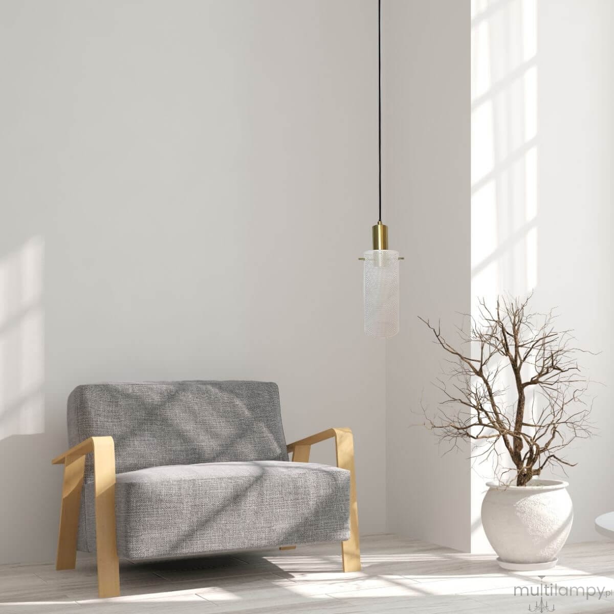 Lampa wisząca Tirana 1xE27 w kolorze złotym i białym, z przezroczystym kloszem, zawieszona na czarnym przewodzie. W tle widoczna szara kanapa z drewnianymi podłokietnikami oraz doniczka z nagim krzewem.