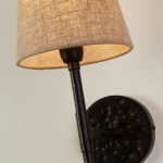 Kinkiet Gothic w czarnym kolorze z abażurem z materiału w odcieniu naturalnego lnu. Lampa zamontowana na ścianie, z prostym, metalowym ramieniem i okrągłą podstawą. Widoczne detale teksturowane na metalowej części.