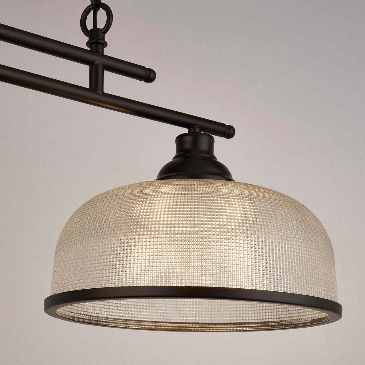 Czarna lampa wisząca Highworth z podwójnym mocowaniem E27. Okrągły, przezroczysty klosz z teksturowanego szkła, metalowa konstrukcja z widocznymi rurkami, zawieszona na łańcuchu. Wymiary i detale konstrukcji podkreślają nowoczesny styl.