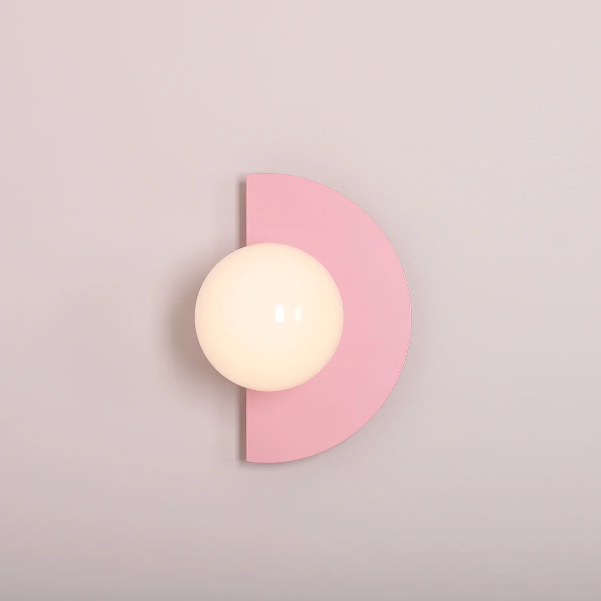 Kinkiet Loop Baby Pink z białą, okrągłą oprawą z mlecznego szkła, umieszczony na różowej, półokrągłej podstawie. Zawieszony na ścianie, idealny do nowoczesnych wnętrz.