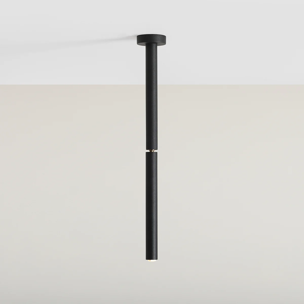 Czarna lampa sufitowa Stick S, 1-punktowa, o minimalistycznym designie. Ułożona pionowo, z metalowym wykończeniem u góry i na dole, zawieszona na białym tle. Idealna do nowoczesnych wnętrz.