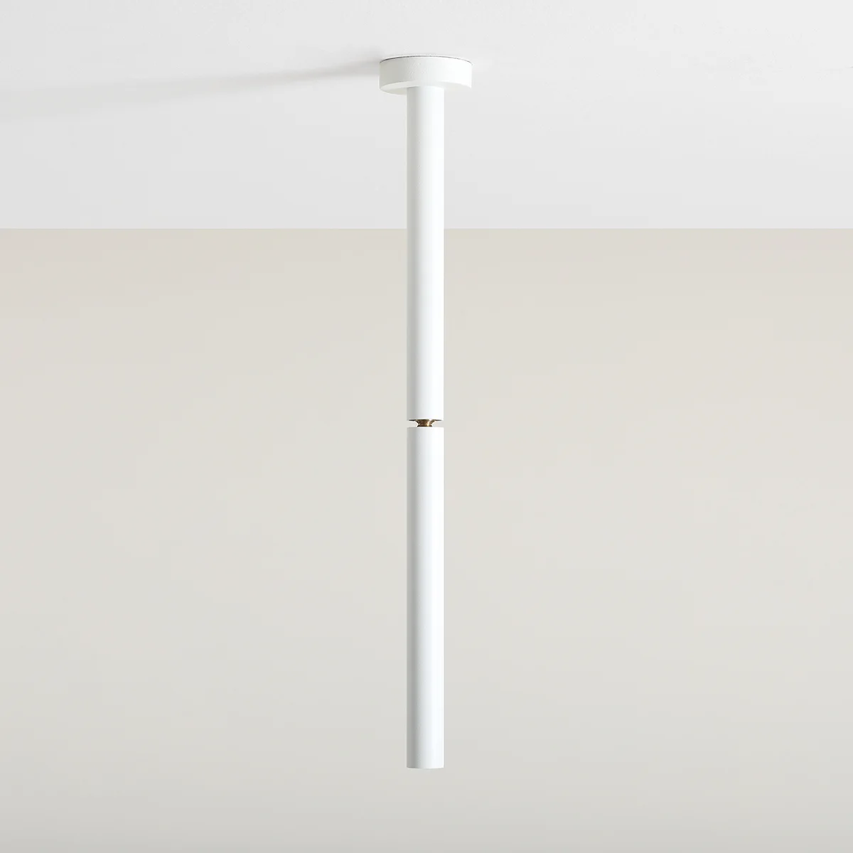 Lampa sufitowa Stick S w kolorze białym, jednolita, o cylindrycznym kształcie. Zawieszona pionowo z metalowym łączeniem w centralnej części. Prosta konstrukcja, idealna do nowoczesnych wnętrz. Tło w odcieniu beżowym.