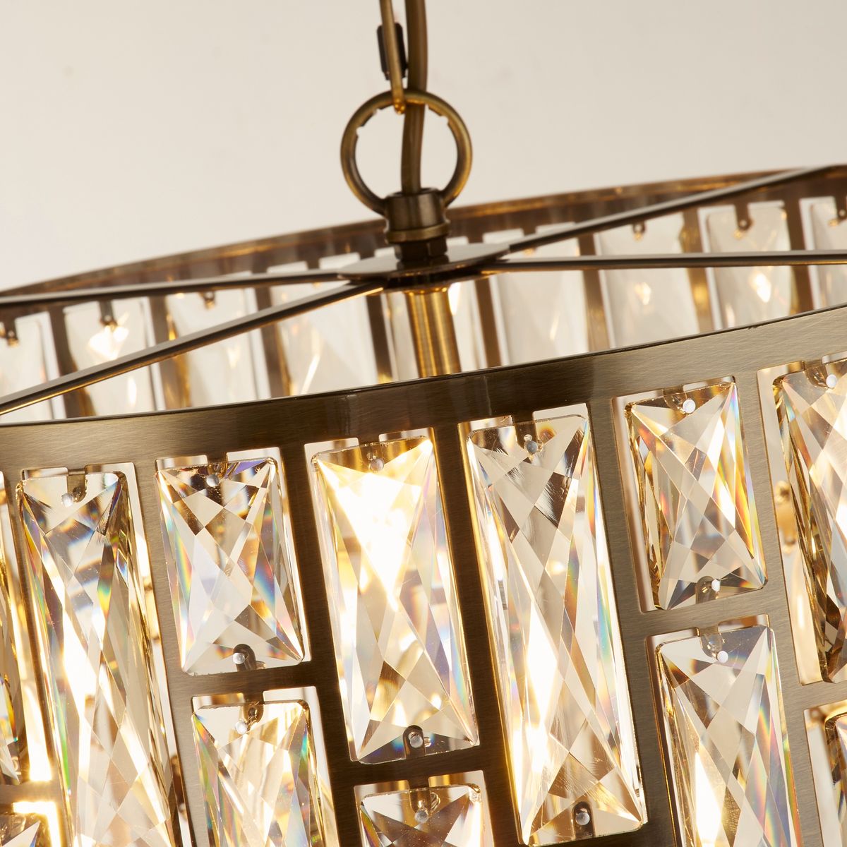 Lampa wisząca Bijou 5xE14 w antycznym mosiądzu, z kryształowymi elementami w formie prostokątów, zawieszona pod kątem. Wnętrze lampy emituje światło, podkreślając błyszczące detale.