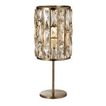 Lampa stołowa Bijou w antycznym mosiądzu z kloszem ozdobionym prostokątnymi kryształami. Ustawiona na okrągłej podstawie, z widocznym miejscem na żarówkę E14. Klosz ma cylindryczny kształt, prezentując elegancki design.