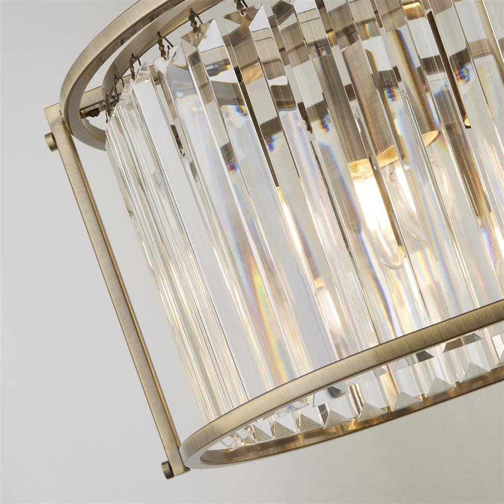 Lampa wisząca Victoria w antycznym mosiądzu, z pięcioma gniazdami E27. Ozdobiona przezroczystymi, prostokątnymi kryształami, tworzy efektowne refleksy świetlne. Ujęcie z boku, ukazujące detale konstrukcji i elementy mocujące.