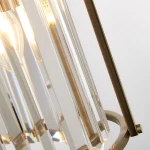 Lampa wisząca Victoria z antycznego mosiądzu, z dwoma oprawami E14. Widoczne przezroczyste klosze z prostokątnymi detalami oraz metalowy stelaż. Ujęcie z boku, ukazujące fakturę i refleksy świetlne.