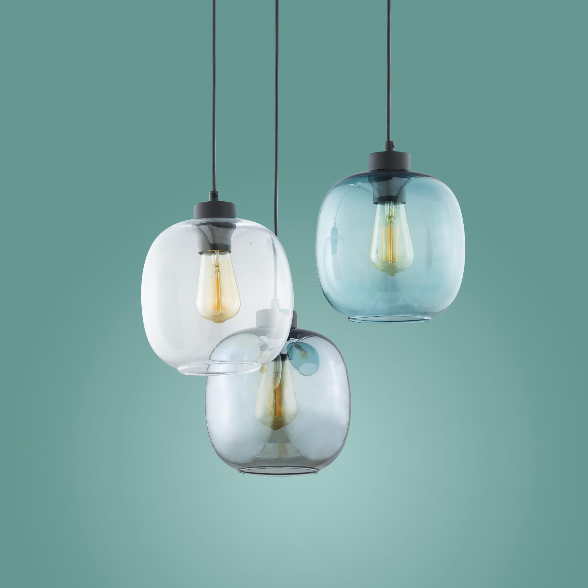 Lampa wisząca Elio 3-punktowa z przezroczystymi i szarymi kloszami o zaokrąglonym kształcie, zawieszona na czarnych przewodach. Widoczne żarówki w stylu retro. Tło w odcieniu zielonym.