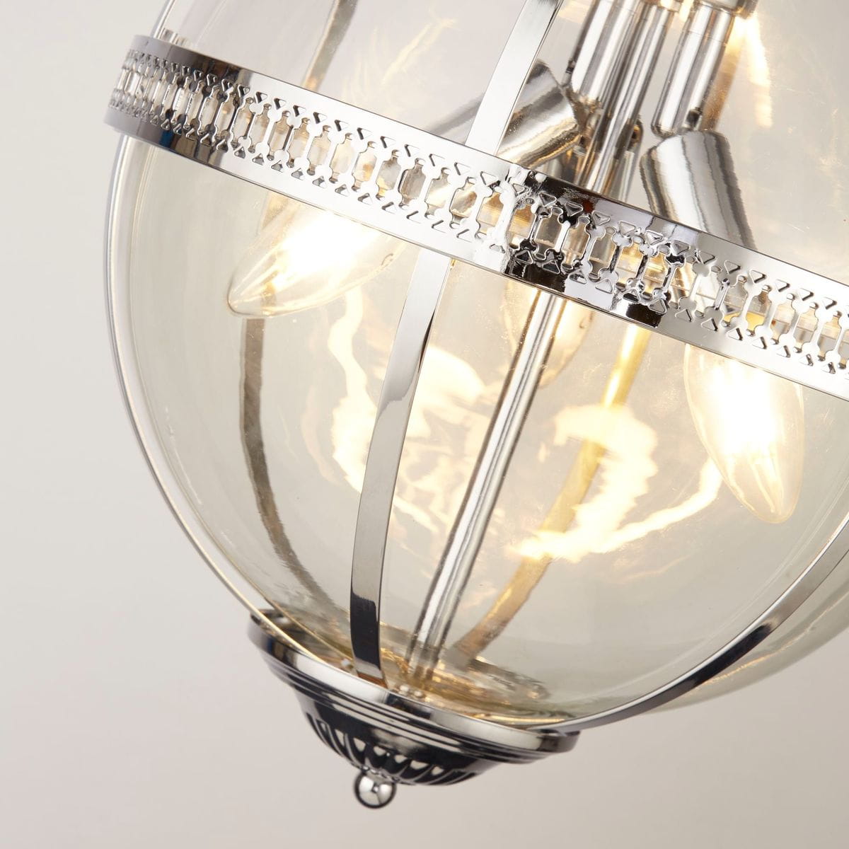Lampa wisząca Coronet 3xE14 w chromowanym wykończeniu. Okrągła, szklana kula z metalową obręczą z wzorem. Widoczne trzy żarówki E14 w środku. Pozycja w zbliżeniu, ukazująca detale konstrukcji i przezroczystość materiału.