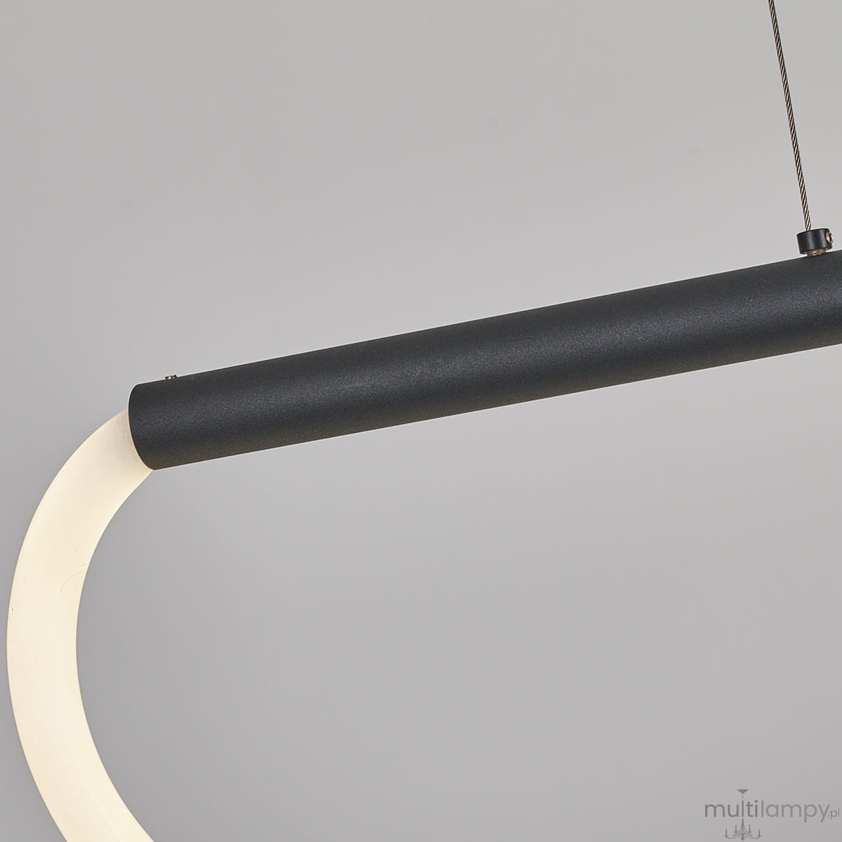 Lampa wisząca Meleca w kolorze czarnym, z pilotem. Konstrukcja z metalowym, matowym uchwytem oraz białym, zakrzywionym kloszem LED. Produkt zamontowany na cienkim, stalowym przewodzie. Tło jasnoszare, podkreślające elegancję lampy.