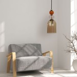 Lampa wisząca Tropea 1xE27 w kolorze czarnym i bursztynowym, z przezroczystym kloszem. Zawieszona na czarnym przewodzie, z dekoracyjnymi elementami w kolorze bursztynowym i różowym. Umieszczona nad szaro-beżową sofą w jasnym wnętrzu.