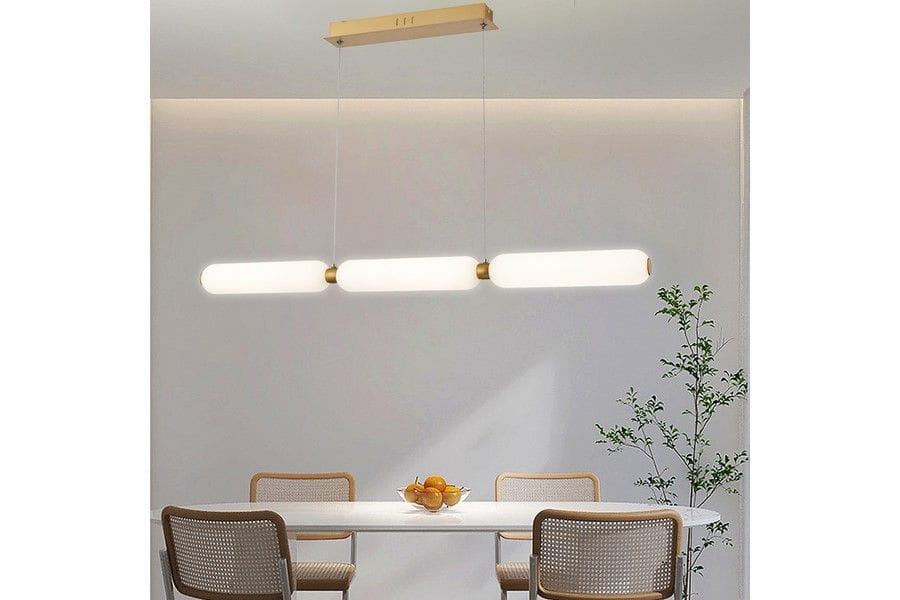 Lampa wisząca Catkin 3xLED/24W w kolorze złotym, z trzema mlecznymi kloszami w kształcie cylindrów. Zawieszona nad białym stołem w jasnym wnętrzu, z drewnianymi krzesłami i rośliną w tle. Kąt ujęcia frontalny, prezentujący całość oświetlenia.