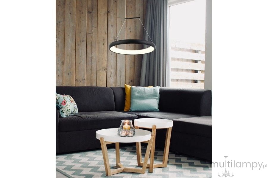 Lampa wisząca Thea D40 w kolorze czarnym, z okrągłym kloszem LED o mocy 24W, zawieszona nad białymi stolikami kawowymi. W tle ciemna sofa z poduszką w kolorze turkusowym i żółtym oraz drewniana ściana.