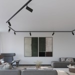 Reflektor spot Reo 1xLED/30W/4000K czarny zamontowany na szynie 3F, skierowany w stronę dwóch abstrakcyjnych obrazów na ścianie. W tle nowoczesne meble w stonowanej kolorystyce.