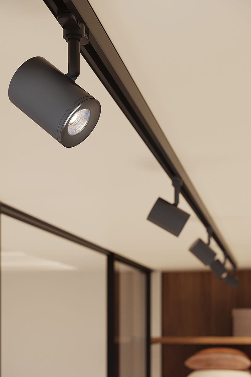 Reflektor Ossi spot 1xGU10 w kolorze czarnym, zamontowany na szynie 3F. Cylindryczny kształt z metalowej obudowy, widoczna soczewka emitująca światło. Ujęcie z boku, w kontekście aranżacji wnętrz.