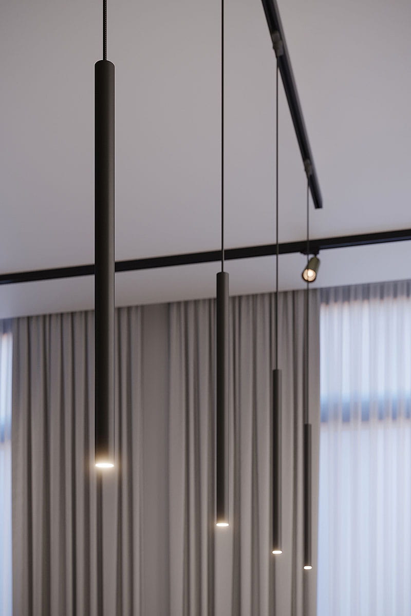 Lampa wisząca Pastelo w kolorze czarnym, zawieszona na długich kablach, składająca się z prostokątnych, cylindrycznych elementów. Ujęcie z boku, ukazujące jasne źródła światła na dole każdego z elementów, w aranżacji z zasłonami w tle.