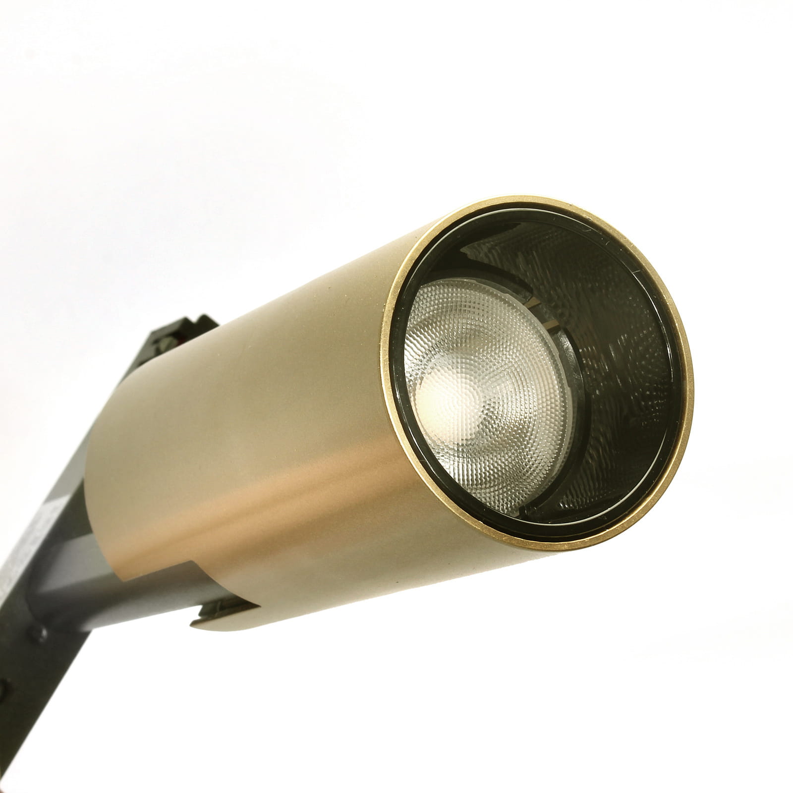 Reflektor spot LED do szyny magnetycznej 7W/4000K w kolorze złotym, o cylindrycznym kształcie, zamontowany pod kątem. Wewnątrz widoczna głowica z soczewką, otoczona metalową obudową. Tło jasne, podkreślające detal i kolor.