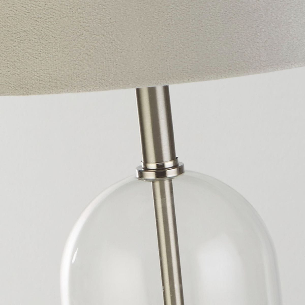 Lampa stołowa Oxford z satynowonickelową podstawą, szarym abażurem z tkaniny i przezroczystą, szklaną częścią. Ujęcie zbliżeniowe na szczegóły konstrukcji, w tym metalowy łącznik między podstawą a kloszem.