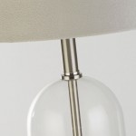 Lampa stołowa Oxford z satynowonickelową podstawą, szarym abażurem z tkaniny i przezroczystą, szklaną częścią. Ujęcie zbliżeniowe na szczegóły konstrukcji, w tym metalowy łącznik między podstawą a kloszem.